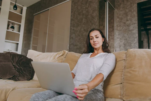 Молодая женщина дома сидит на диване, отдыхает в гостиной и работает с ноутбуком — стоковое фото