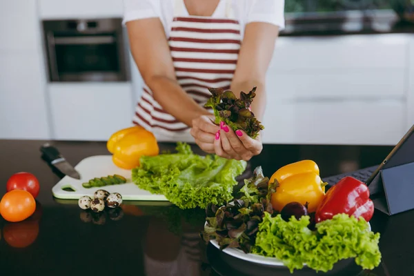 Молодая счастливая женщина держит овощи в руках на кухне с ноутбуком на столе. Овощной салат. Концепция диеты. Здоровый образ жизни. Готовить дома. Приготовьте еду. . — стоковое фото