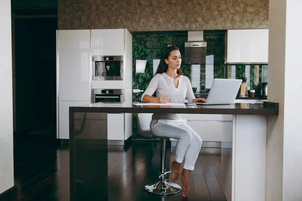 Attraente giovane donna d'affari moderna che lavora con documenti e laptop in cucina a casa — Foto Stock