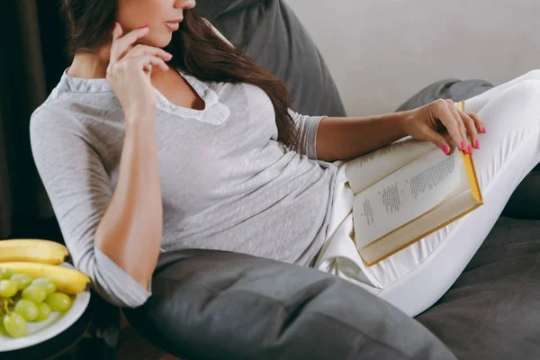 Mulher bonita em casa sentada na cadeira moderna em frente à janela, relaxando em sua sala de estar e livro de leitura. Fechar — Fotografia de Stock