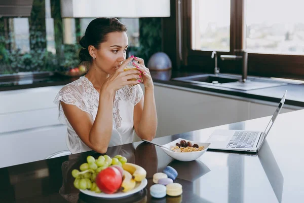 Портрет красивой молодой женщины, работающей с ноутбуком за завтраком с зерновыми, молоком и апельсиновым соком. Еда дома . — стоковое фото