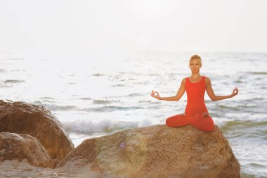 Pratik yoga taş gündoğumu deniz kenarında, Kırmızı elbiseli bir kadın