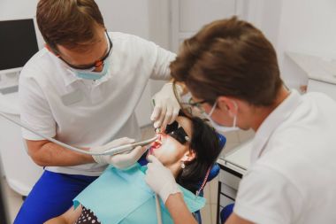 Bir kadın yardımcı erkek bir dişçiyle ofiste bir klinik bir kadın hastada diş tedavisinde yardımcı olur