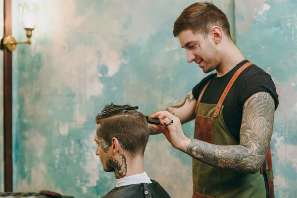 Close up shot of man getting trendy haircut at barber shop. Male hairstylist in tattoos serving client. — Stock Photo, Image