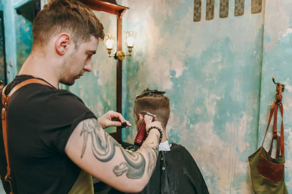 Крупный план человека, стригущегося в парикмахерской. Мужчина-парикмахер в татуировках обслуживающий клиента . — стоковое фото