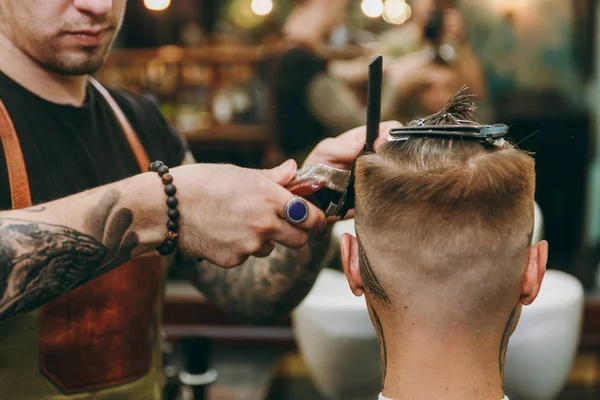 Крупный план человека, стригущегося в парикмахерской. Мужчина-парикмахер в татуировках обслуживающий клиента . — стоковое фото