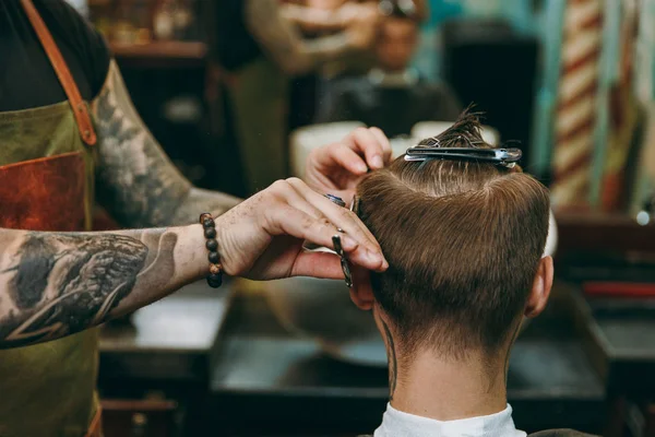 Nära upp skott av mannen få trendiga frisyr på frisör. Manlig Frisör i tatueringar som betjänar klienten. — Stockfoto