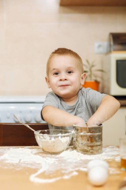 Küçük çocuk çocuk anne Noel ışık mutfakta zencefilli bisküvi pişirmek için yardımcı olur. Gri T-shirt hafta sonu sabah evde masada demir elek ve un ile 2-3 yıl içinde mutlu sarışın çocuk.