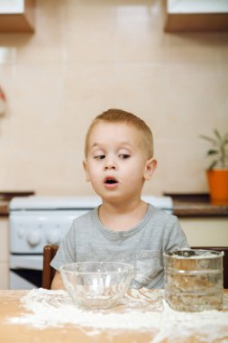 Küçük çocuk çocuk anne Noel ışık mutfakta zencefilli bisküvi pişirmek için yardımcı olur. Gri T-shirt hafta sonu sabah evde masada demir elek ve un ile 2-3 yıl içinde mutlu sarışın çocuk.