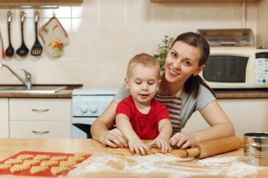 Küçük çocuk çocuk anne Noel ışık mutfakta zencefilli bisküvi pişirmek için yardımcı olur. Mutlu aile anne 30-35 yıl ve 2-3 rulo dışarı hamur ve çerezler de uygunbir çocuk ev. İlişki ve sevgi kavramı