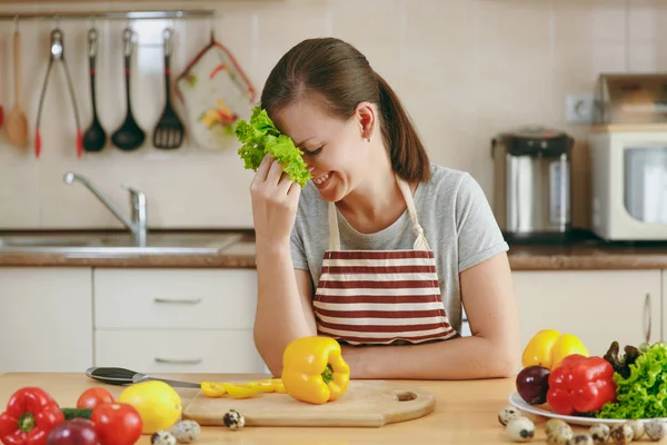 Молодая привлекательная женщина в фартуке с листьями салата, смеющаяся на кухне. Концепция диеты. Здоровый образ жизни. Готовить дома. Готовьте еду. . — стоковое фото