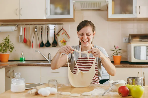 Молодая веселая веселая и улыбающаяся женщина надевает тесто с дырками на лице и веселится на кухне. Готовлю дома. Готовьте еду. . — стоковое фото