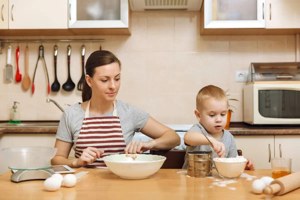 Little kid boy helps mother to cook Christmas ginger biscuit in light kitchen with tablet on the table. Happy family mom 30-35 years and child 2-3 in weekend morning at home. Relationship concept — Stock Photo, Image