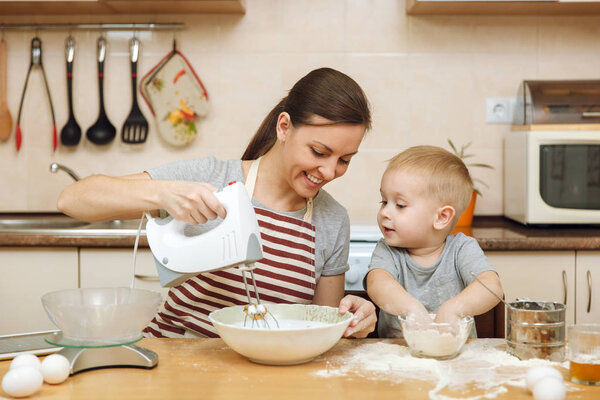 Маленький мальчик помогает маме готовить рождественское имбирное печенье на светлой кухне с табличкой на столе. Счастливая семейная мама 30-35 лет и ребенок 2-3 в выходные утром дома. Концепция отношений
