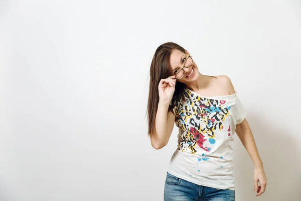 Hermosa joven europea sonriente mujer de cabello castaño con una piel sana y limpia, vestida con ropa casual de pie con gafas para la vista sobre un fondo blanco. Concepto de emociones . —  Fotos de Stock