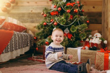Mutlu sevimli küçük erkek bebek kazak ve ahşap Oda evde oyuncaklar ile Noel ağacı süsleme kot pantolon giymiş. Çocuk iyi bir ruh hali ile. Yeni yıl. Yaşam tarzı, Aile ve tatil 2018 kavramı