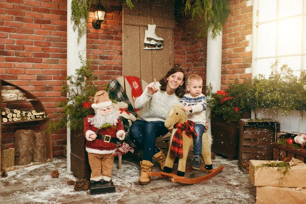 Νεαρή ευτυχισμένη μητέρα με ένα χαριτωμένο μικρό παιδί αγόρι άλογο λικνίσματος, ντυμένος με πουλόβερ σε διακοσμημένο νέο έτος της δωμάτιο με Santa στο σπίτι. Χριστούγεννα καλή διάθεση. Τρόπου ζωής, οικογένεια και διακοπές έννοια 2018 — Φωτογραφία Αρχείου