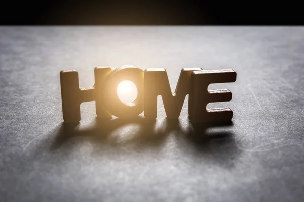 Word Home di lettere in legno su una texture scura con sfondo nero con retroilluminazione. Effetto luce . — Foto Stock