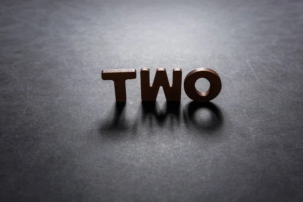 Word Two of wooden letters on a dark texture with a black background with backlight. Lighting effect. — Stock Photo, Image