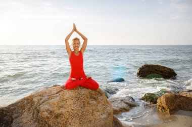 Pratik yoga taş gündoğumu deniz kenarında, Kırmızı elbiseli bir kadın