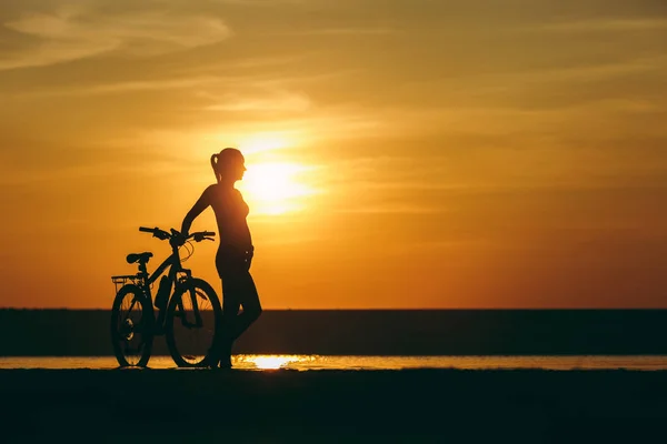 Silhouette of a sporty girl in a suit standing near a bicycle in — Stock Photo, Image