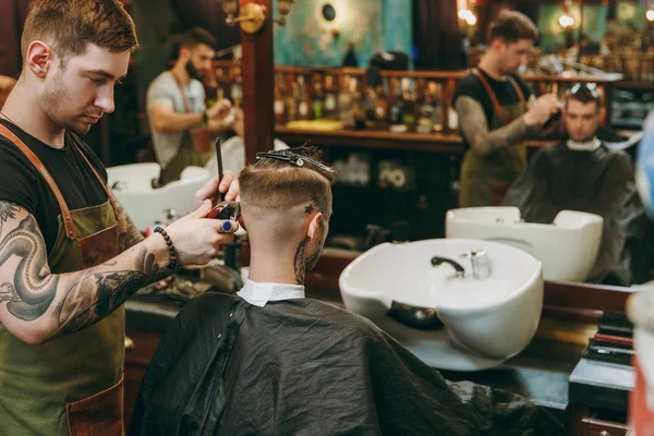 Ein Mann, der sich beim Friseur eine modische Frisur schneidet. männlicher Friseur mit Tätowierungen im Dienste des Kunden. — Stockfoto