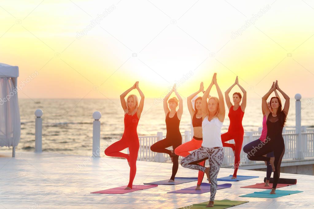 A group of women doing yoga at sunrise near the sea