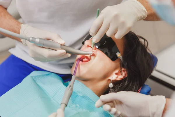 En manlig tandläkare med en kvinnlig assistent hjälper till att behandla tänderna hos en kvinnlig patient i en klinik i kontoret, närbild — Stockfoto