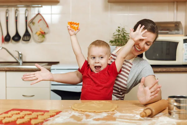 Jongen-jongetje helpt moeder om te koken kerst gember koekje in lichte keuken. Gelukkige familie moeder 30-35 jaar en kind 2-3 roll-out deeg en uitgesneden cookies op thuis. Relatie en liefde concept — Stockfoto