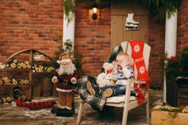 Oynak mutlu sevimli küçük çocuk çocuk kazak ve Noel Baba evde dekore edilmiş yeni yıl odasında sandalye üzerinde oturan kot pantolon giymiş. Noel keyfi. Yaşam tarzı, Aile ve tatil 2018 kavramı