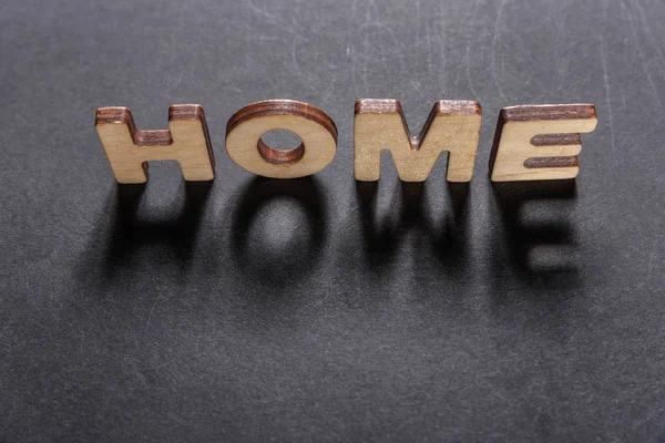 Word Home di lettere in legno su una texture scura con sfondo nero con retroilluminazione. Effetto luce . — Foto Stock