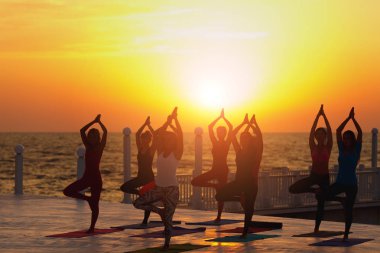 Bir grup kadın gündoğumu deniz kenarında, yoga yaparken