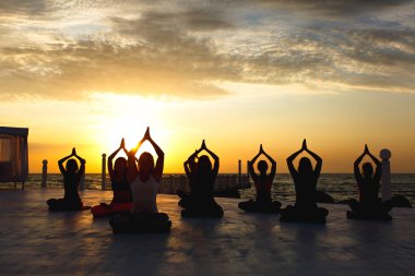 Bir grup kadın gündoğumu deniz kenarında, yoga yaparken