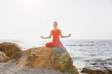 Pratik yoga taş gündoğumu deniz kenarında, Kırmızı elbiseli bir kadın