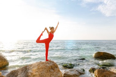 Pratik yoga taş gündoğumu deniz kenarında, Kırmızı elbiseli bir kadın