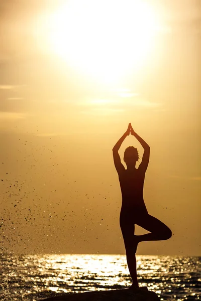 Pratik yoga taş gündoğumu deniz kenarında, Kırmızı elbiseli bir kadın