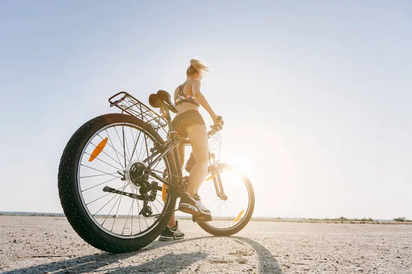 A strong blonde woman in a multicolored suit sits on a bicycle i — Stock Photo, Image