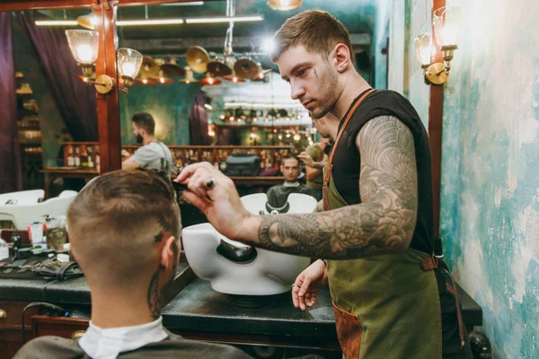 Крупним планом чоловік стає модною стрижкою в перукарні. Чоловічий перукар в татуюваннях, що обслуговують клієнта . — стокове фото