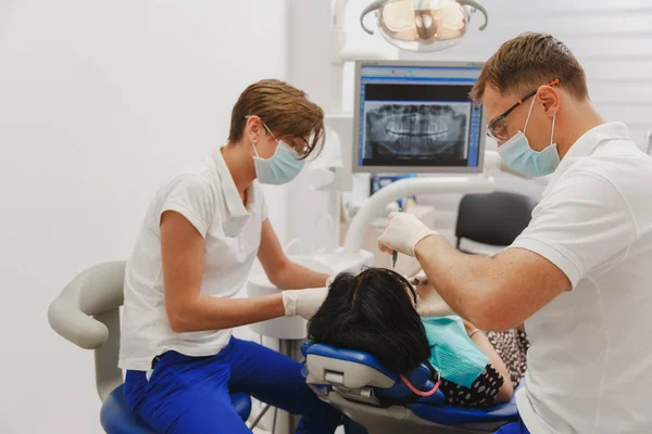 En manlig tandläkare med en kvinnlig assistent hjälper till att behandla tänderna hos en kvinnlig patient på klinik på kontoret — Stockfoto
