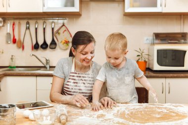 Küçük çocuk çocuk anne Noel masanın üzerine tablet ile ışık mutfakta zencefilli bisküvi pişirmek için yardımcı olur. Mutlu aile anne 30-35 yıl ve çocuk 2-3 hafta sonu sabah evde. İlişki kavramı