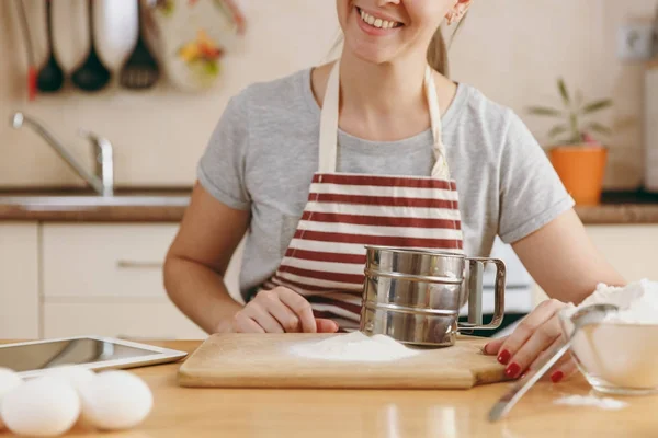 Молодая улыбающаяся женщина с железным решетом и мукой на столе на кухне. Готовлю дома. Готовьте еду. . — стоковое фото