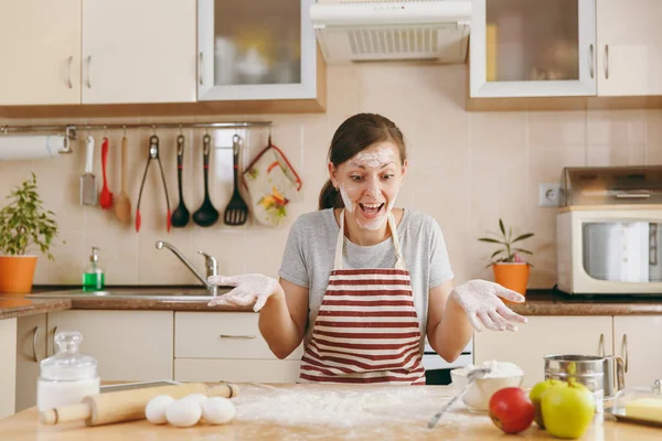 Uma mulher alegre engraçada nova que senta-se em uma mesa com farinha e vai preparar uns bolos de Natal na cozinha. A cozinhar para casa. Preparar alimentos . — Fotografia de Stock