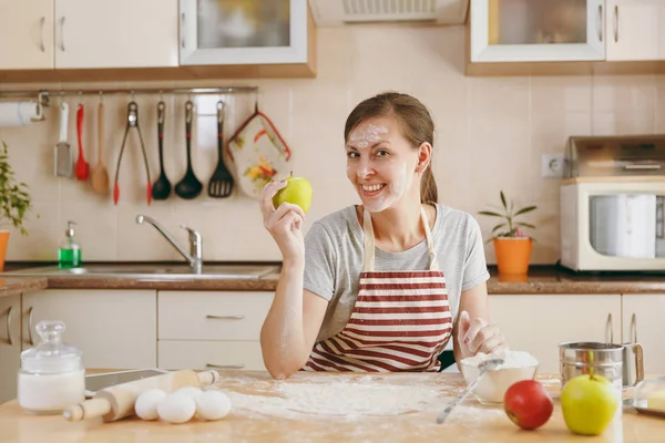 Uma jovem bela mulher feliz sentada a uma mesa com farinha e vai preparar um bolo de Natal na cozinha. A cozinhar para casa. Preparar alimentos . — Fotografia de Stock