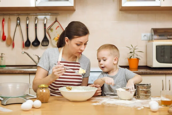 Little kid boy helps mother to cook Christmas ginger biscuit in light kitchen with tablet on the table. Happy family mom 30-35 years and child 2-3 in weekend morning at home. Relationship concept — Stock Photo, Image