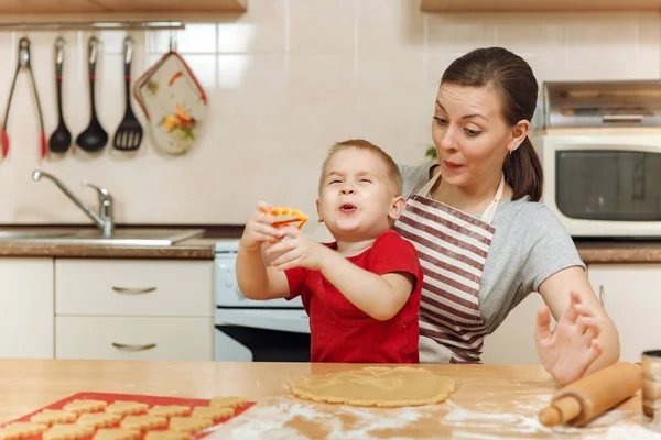Jongen-jongetje helpt moeder om te koken kerst gember koekje in lichte keuken. Gelukkige familie moeder 30-35 jaar en kind 2-3 roll-out deeg en uitgesneden cookies op thuis. Relatie en liefde concept — Stockfoto