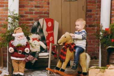 Oynak mutlu sevimli küçük çocuk çocuk kazak ve sallanan at odasında dekore edilmiş yeni yıl Noel Baba evde oturan kot pantolon giymiş. Noel keyfi. Yaşam tarzı, Aile ve tatil 2018 kavramı