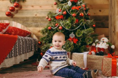 Mutlu sevimli küçük erkek bebek kazak ve ahşap Oda evde oyuncaklar ile Noel ağacı süsleme kot pantolon giymiş. Çocuk iyi bir ruh hali ile. Yeni yıl. Yaşam tarzı, Aile ve tatil 2018 kavramı