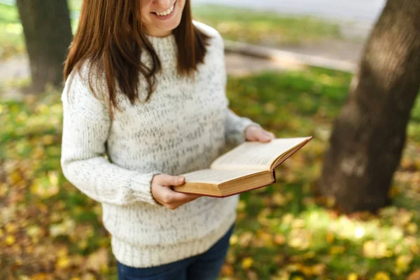 Piękny szczęśliwy uśmiechający się Brunet Kobieta w stały sweter biały czerwony książkę w Upadek miasta park na ciepły dzień. Autumn golden odchodzi. Koncepcja czytania. — Zdjęcie stockowe