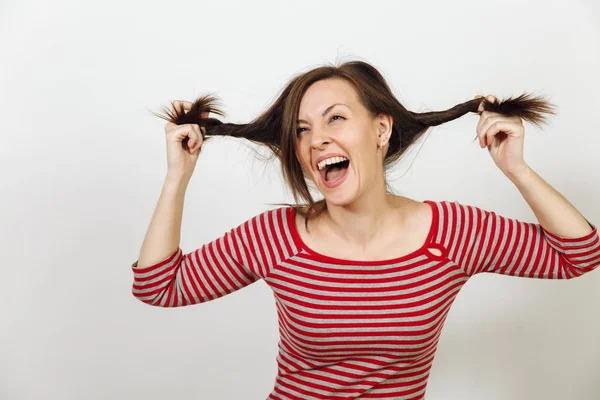 Bella giovane donna europea dai capelli castani felice con una pelle sana e pulita e un sorriso affascinante, vestita con abiti casual rossi e grigi, ingannando e ridendo su uno sfondo bianco. Concetto di emozioni . — Foto Stock