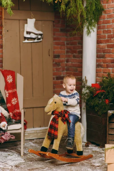 Playful smiling happy cute little child boy dressed in sweater and jeans sitting on rocking horse in decorated New Year room at home. Christmas good mood. Lifestyle, family and holiday 2018 concept